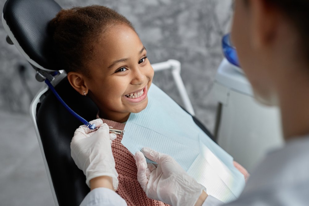 Portrait of cute black girl in dental chair with nurse or dentist preparing her for teeth exam, copy space - DeMoss Pediatric Dentistry | Dentist Englewood Ohio